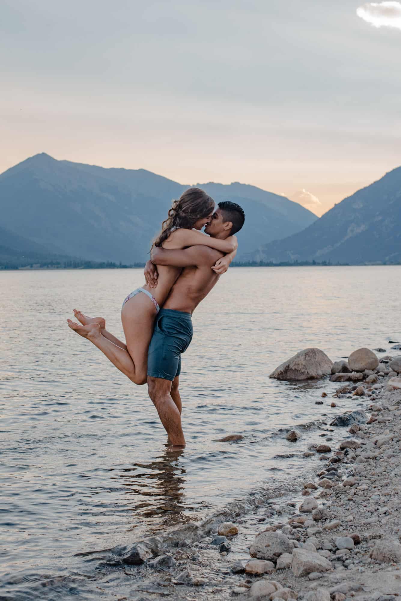 female being lifted out of an alpine lake by male holding her up as her hands are wrapped around his neck and the sun has set behind them, joyful for following this simple proposal idea and denver proposal idea list to have a magical time together