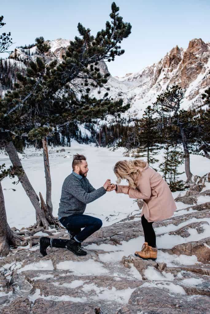 male bending down on one knee asking his girl to marry her in the mountains at sunrise, after working with emmy of Celebrate Again thinking of simple proposal ideas and denver proposal ideas