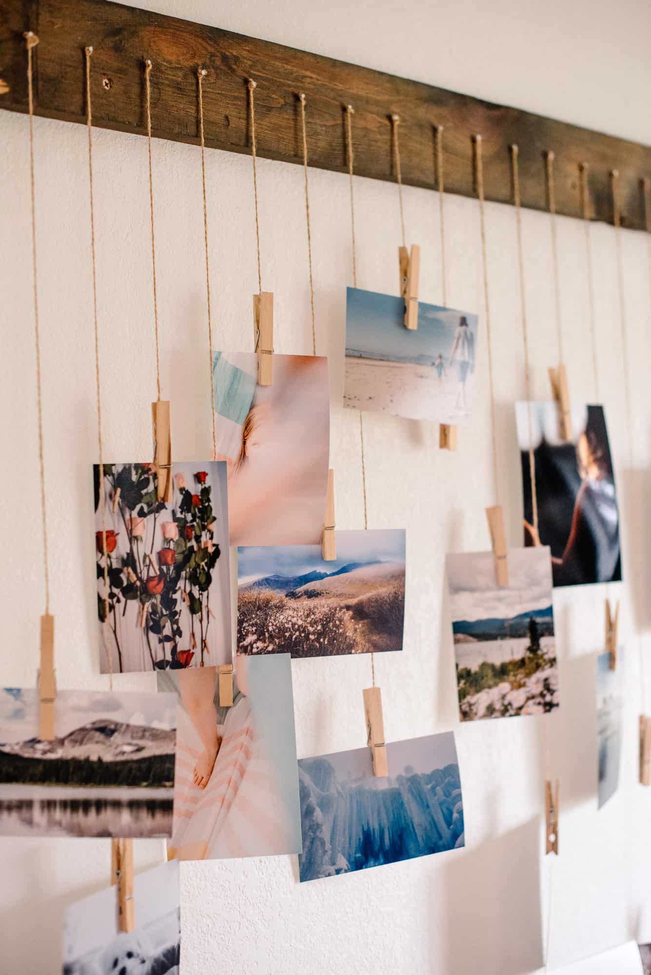 many photos hanging by string clipped on a clothes pin hanging from string on a nail on a wood board