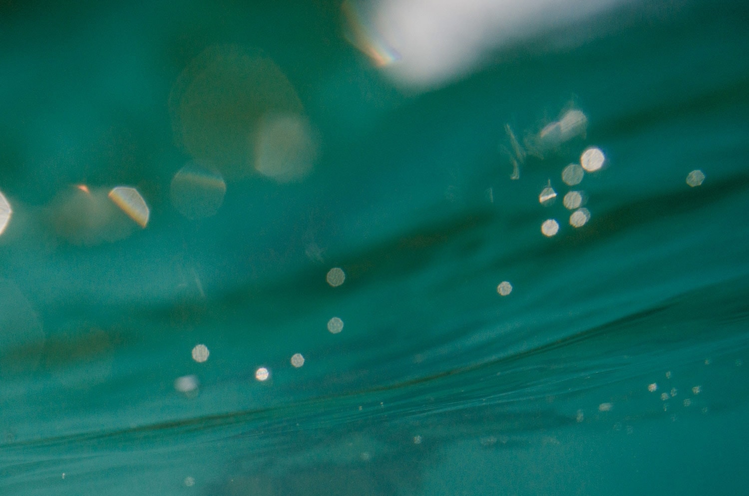 turquoise photo of under the water with white circles making water bubbles