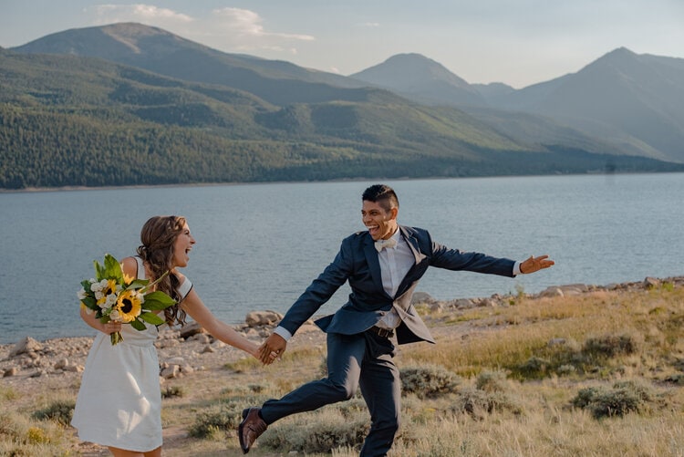 bride and groom running on their wedding day in the mountains laughing
