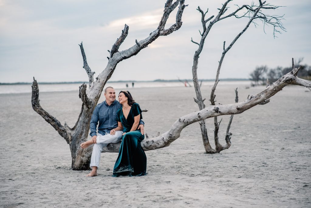 couple sitting on dead tree on folly beach laughing