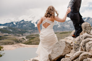 bride in her elopement wedding dress walking up rocks in mountains while holding her spouses hand.
