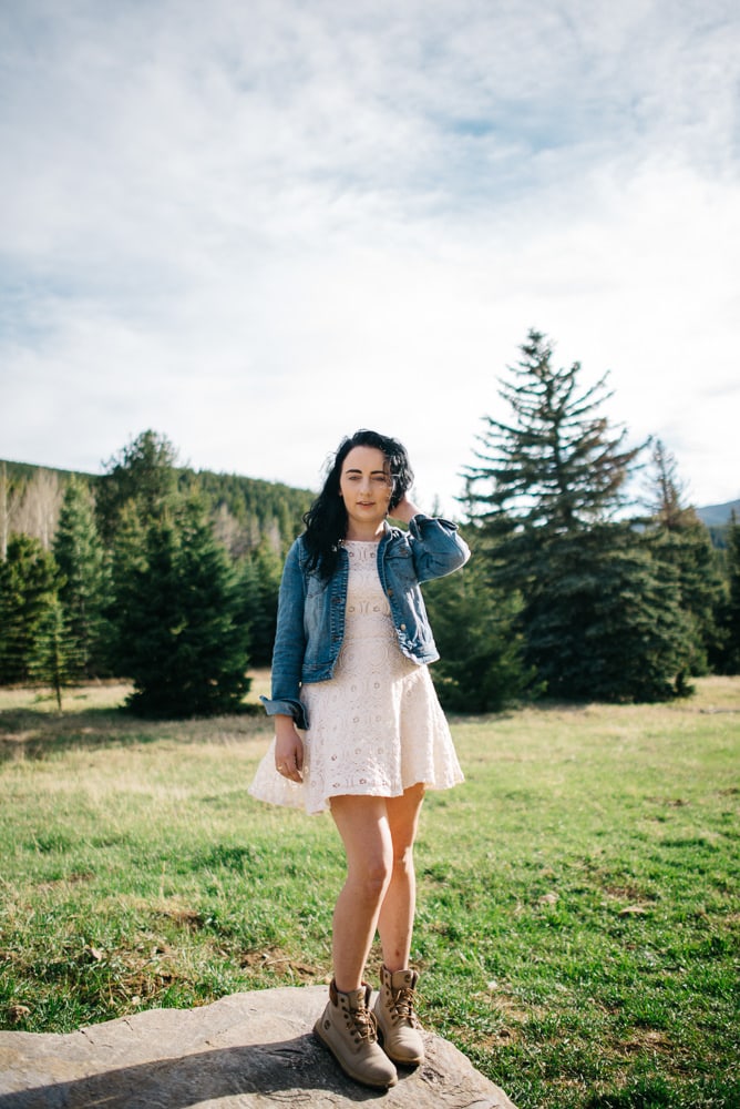 bride in tea length wedding dress and hiking boots with a jean jacket standing on a rock in the mountains