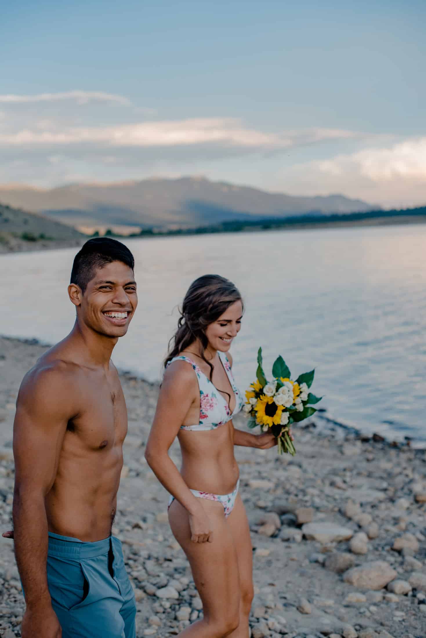couple in swimsuits, bride holding flowers as they walk down to the beach for a swim