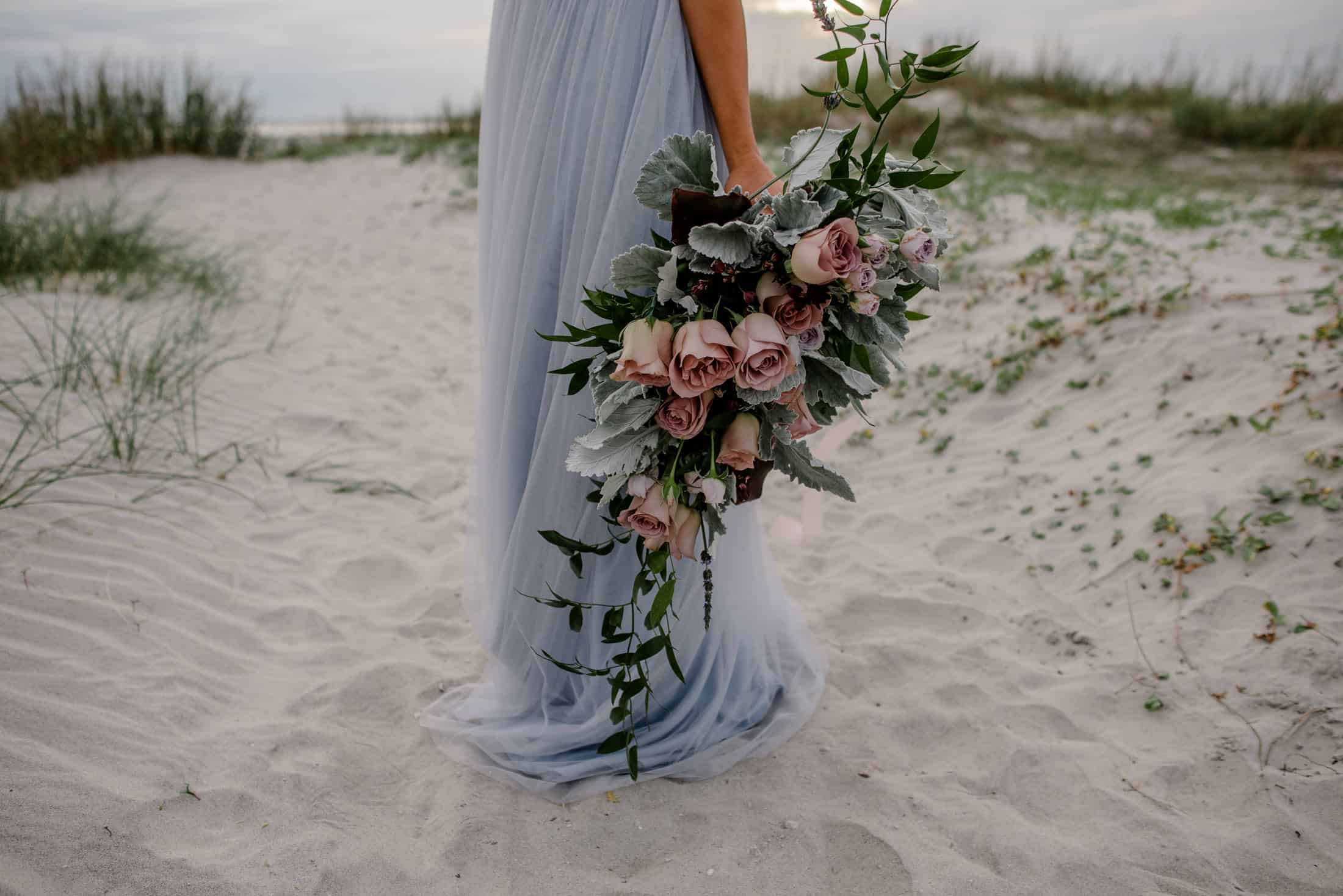 bride holding her flowers down as they drape with her dress as she has a Cannon Beach Elopement