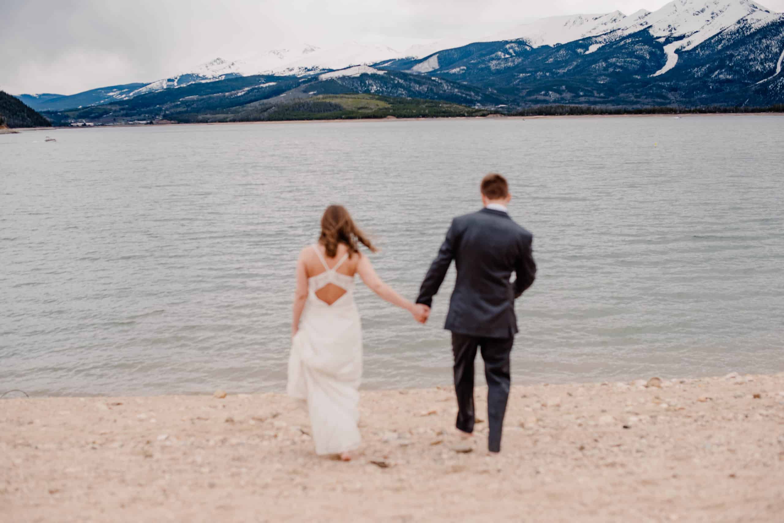 couple running away holding hands barefoot near alpine lake