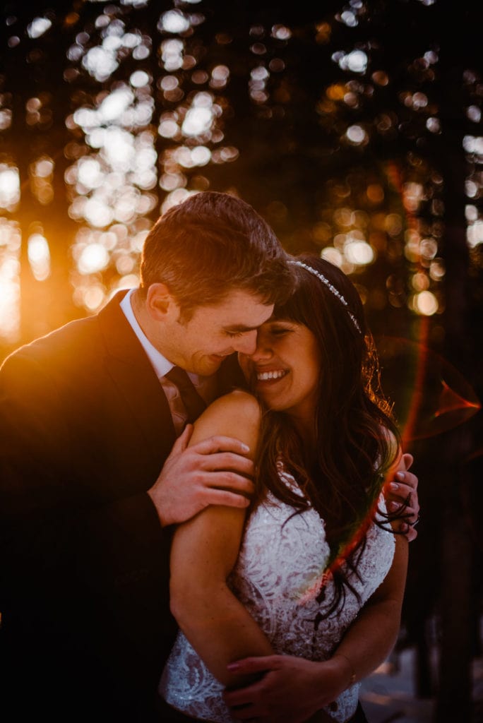 couple snuggling as light leaks through in the forest