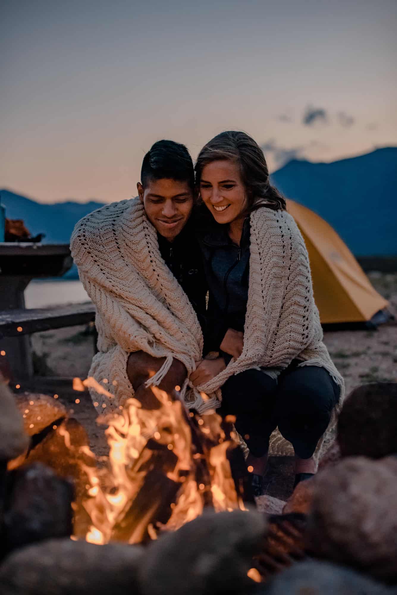 couple enjoying a camp fire snuggled up in a blanket together