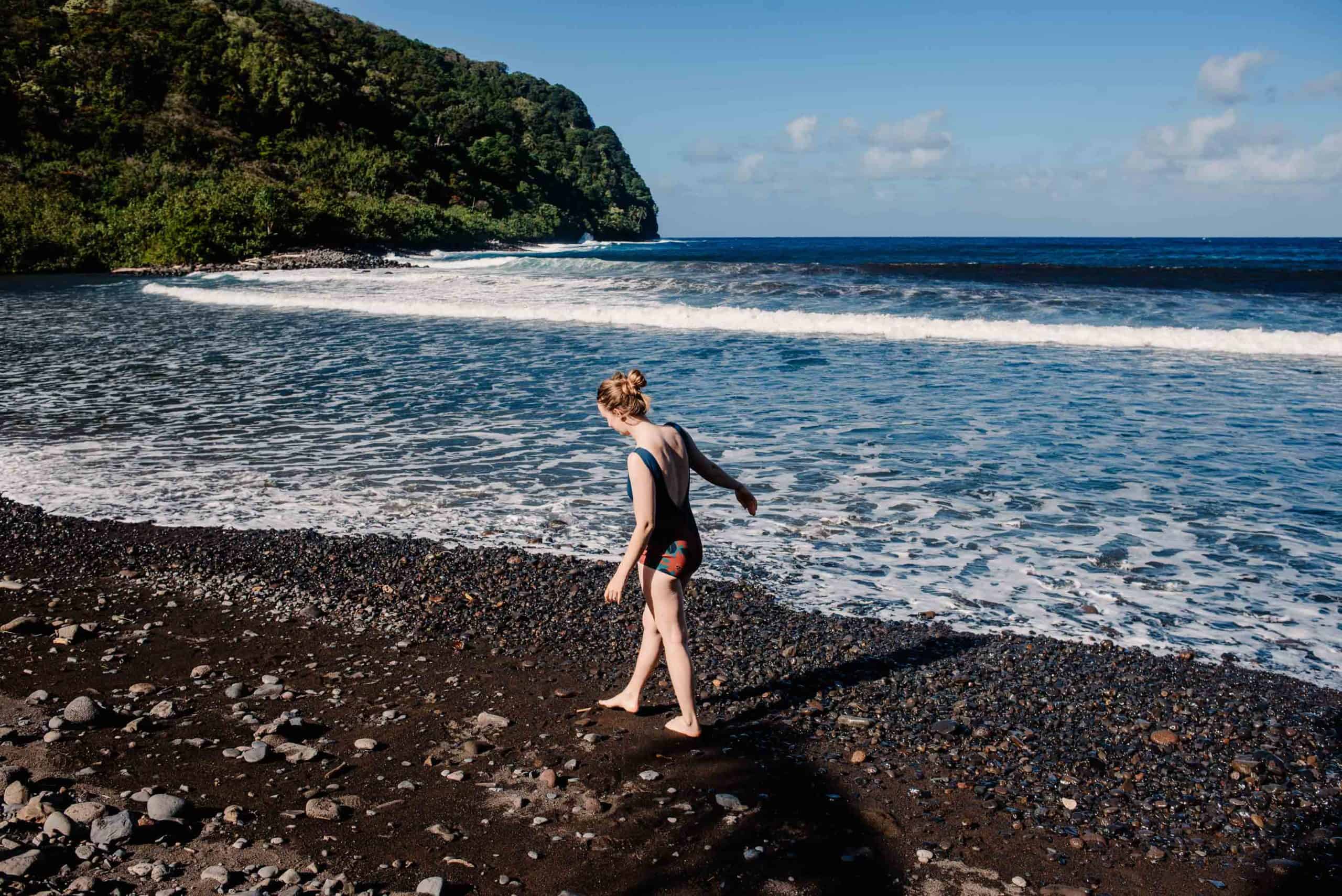 female walking along the black sand beach in Maui in her Seea Swimsuit