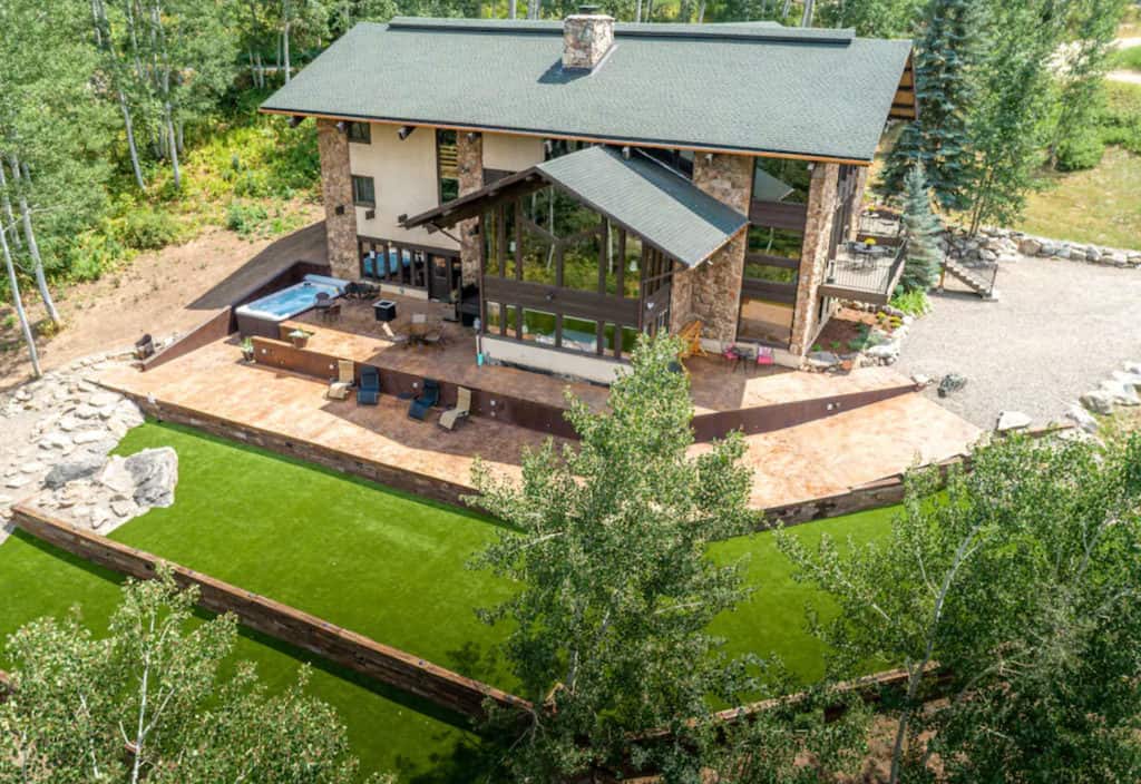 ariel view of large luxurious home with green grass, tress and patio decks and hot tub in view