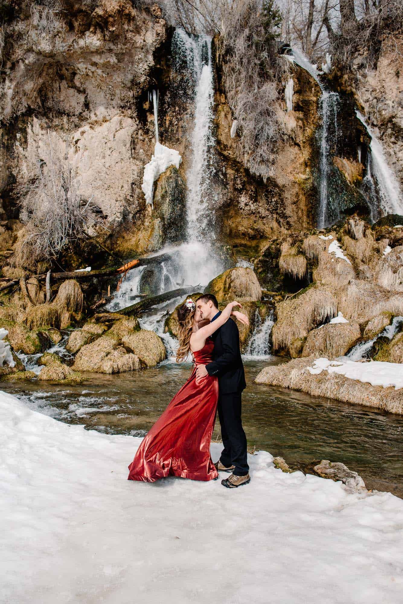 bride and groom kissing in front of an epic waterfall during winter who are eloping during the pandemic