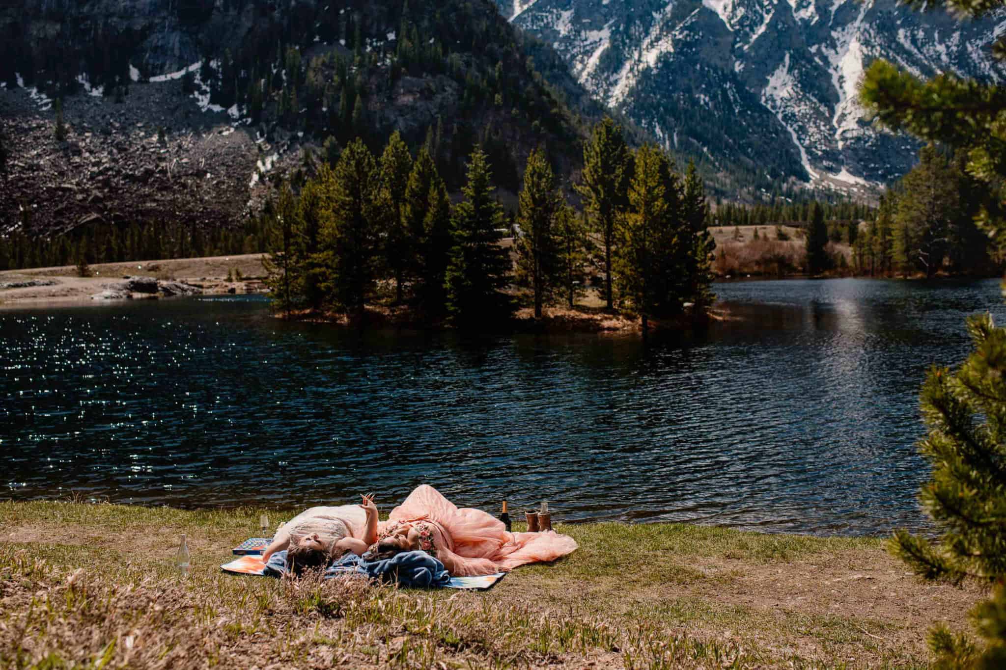 couple sitting on a blanket enjoying a romantic wedding day picnic with mountains in the background