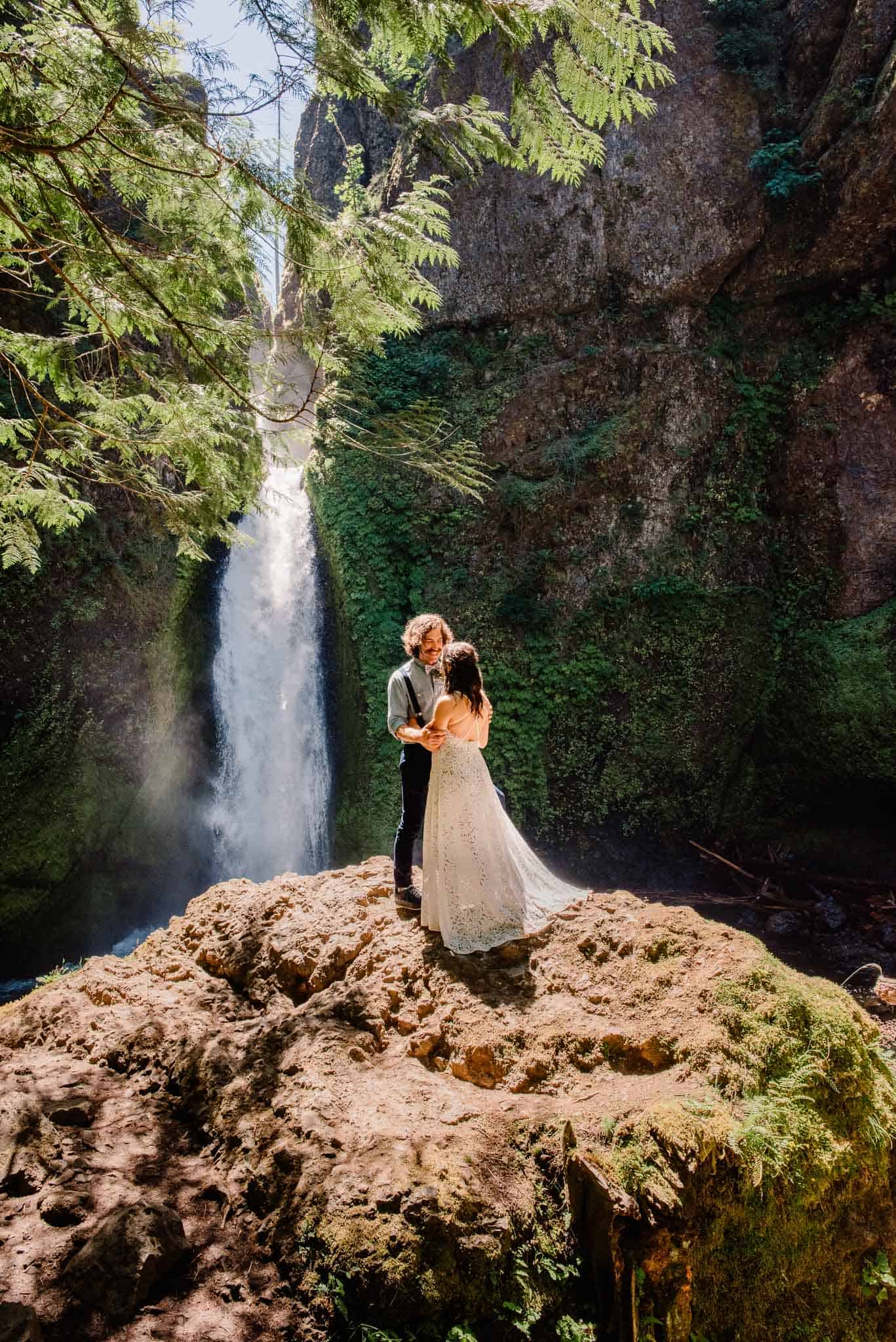 bride and groom standing on a rock with the bride and groom exchanging rings at Wahclella Falls behind them after their Wahclella falls wedding