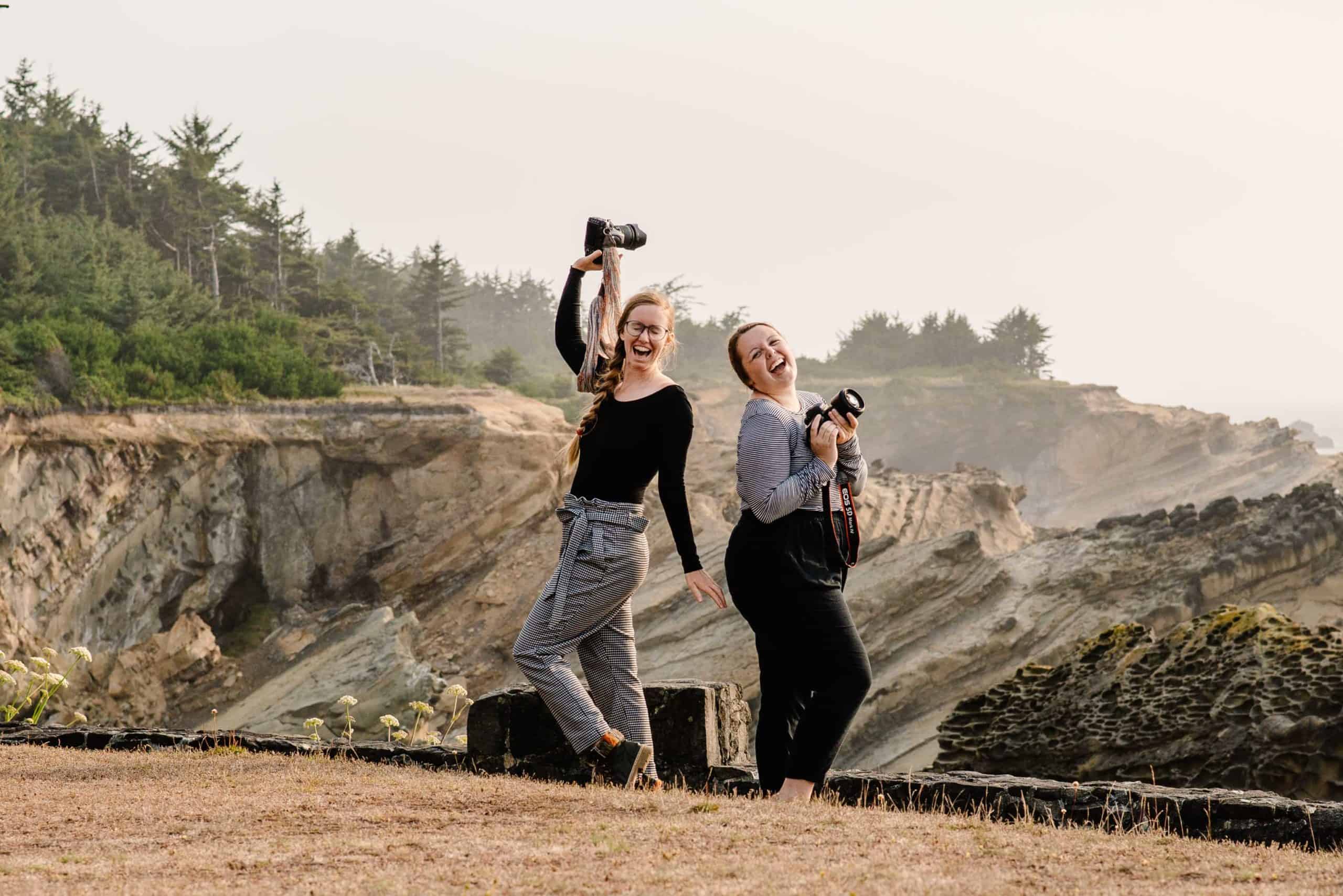 Emmy and Liv from Celebrate Again standing on the Oregon Coast with their cameras raised laughing