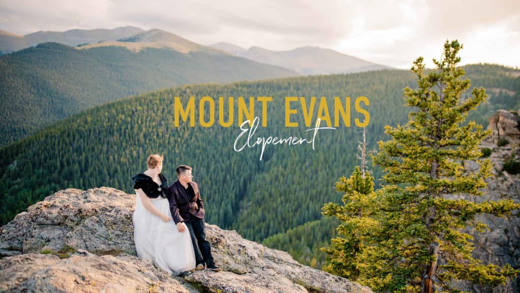 "Mount Evans elopement" couple sitting on a rock with a tree in the foreground and mount evans in the background on their wedding day