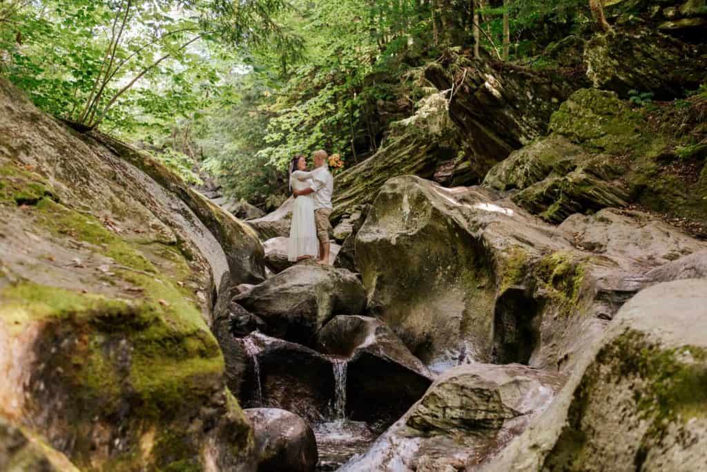 couple in a river bed with a little waterfall by them photo by Mirona Photography
