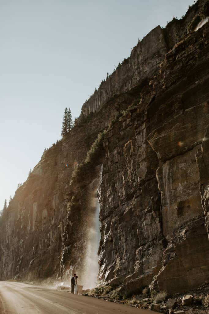 Going to the sun road falls are illuminated by golden hour as a couple in wedding attire explores this waterfall wedding venue.