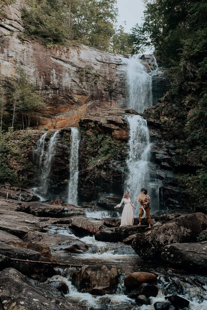 couple walking on rocks with a waterfall wedding venue High Falls behind them photo by Flit Photography