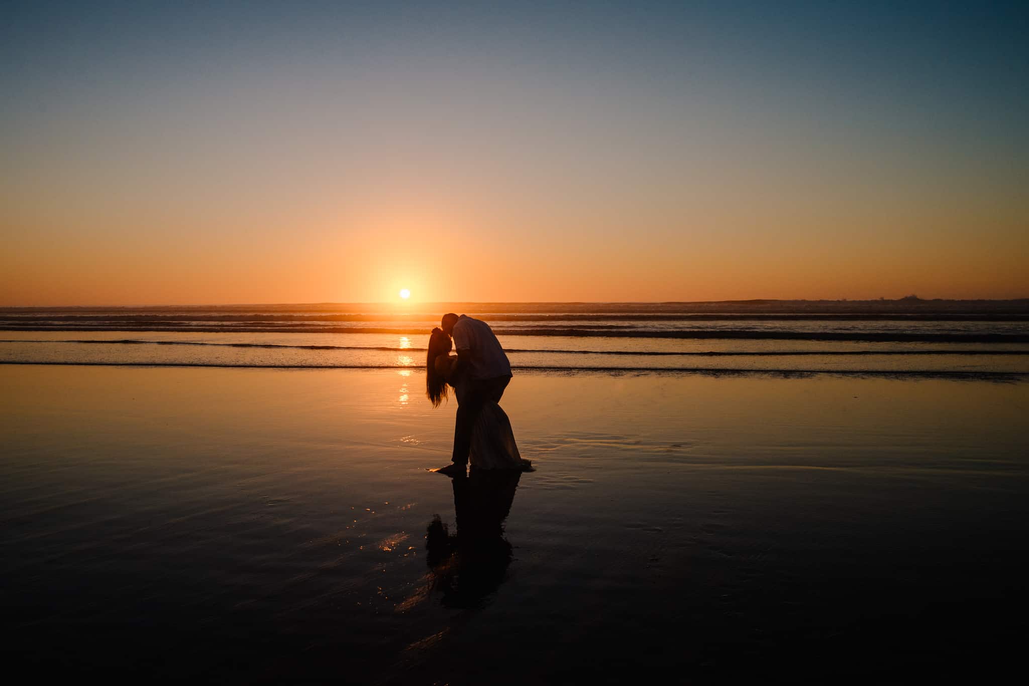 couple silhouetted by sunset on the beach as their Hawaii elopement photographer takes their photo