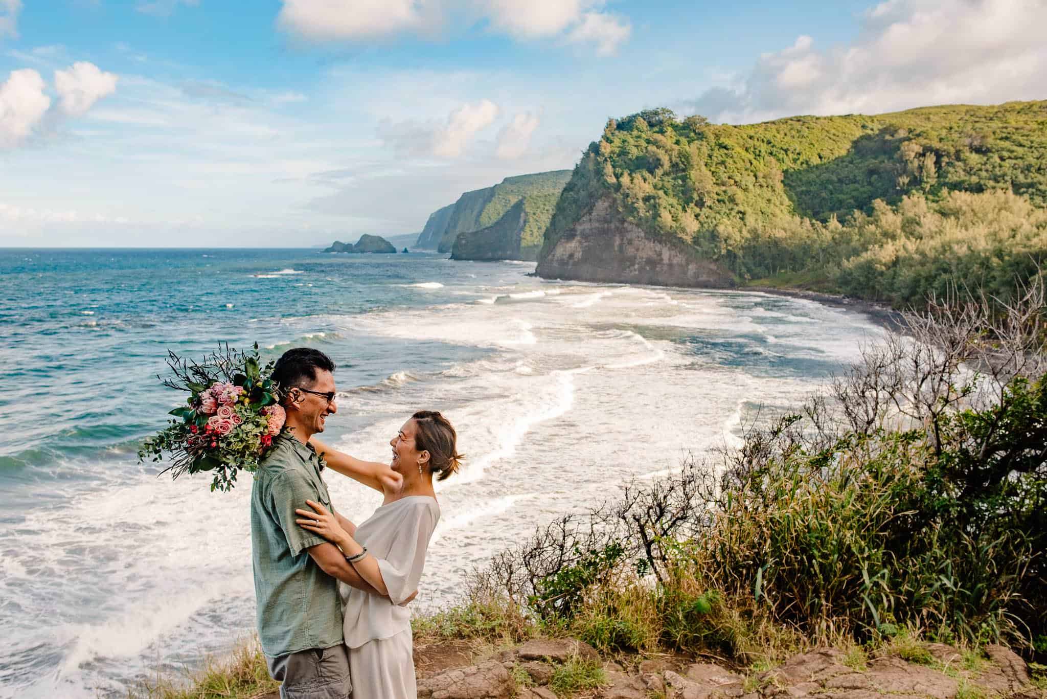 couple smiling at each other with the Pacific ocean in the background and a mountain valley that meets the ocean as their Hawaii elopement photographer takes their photo