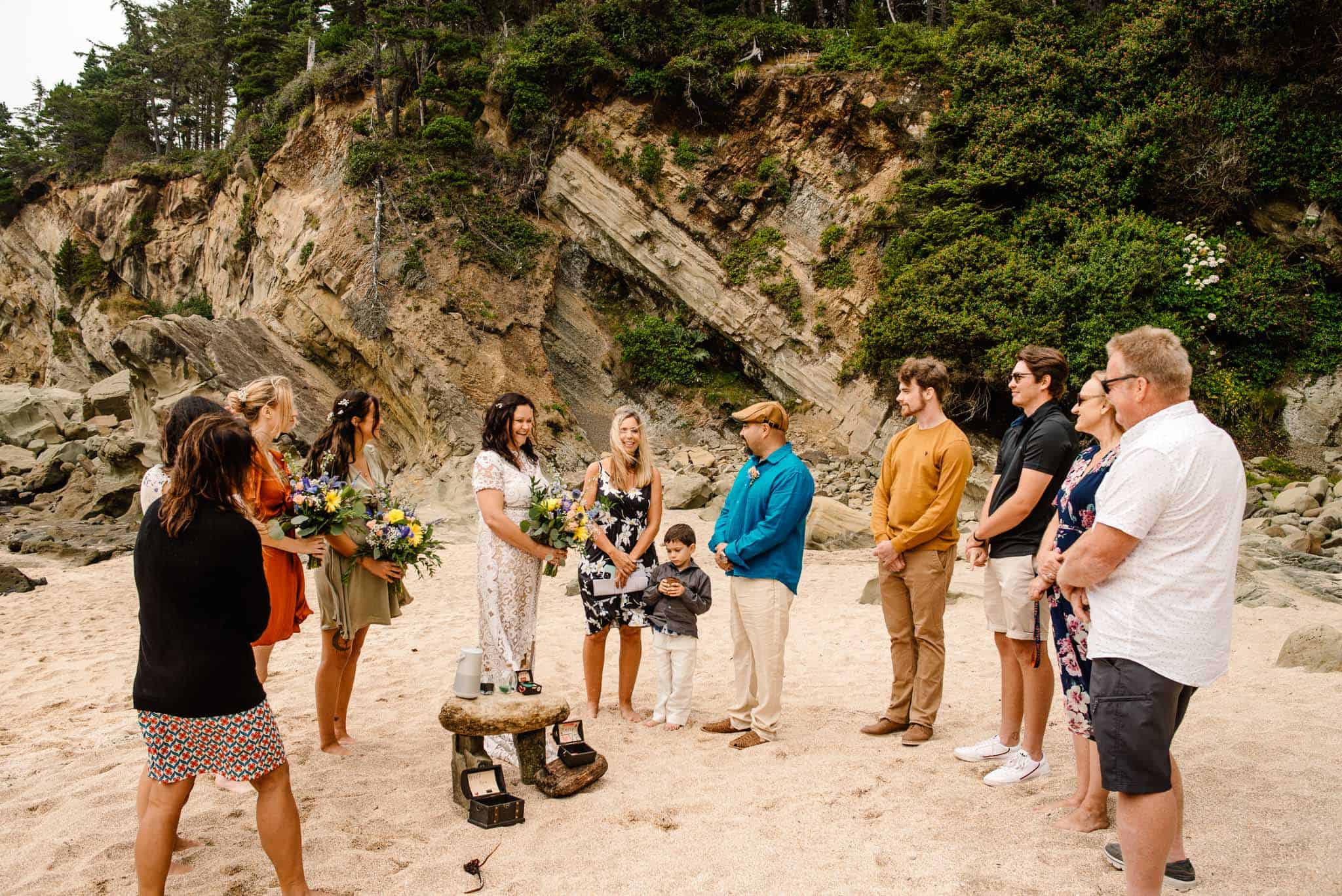 couple eloping with family standing around them on a sandy beach and cliff in the background