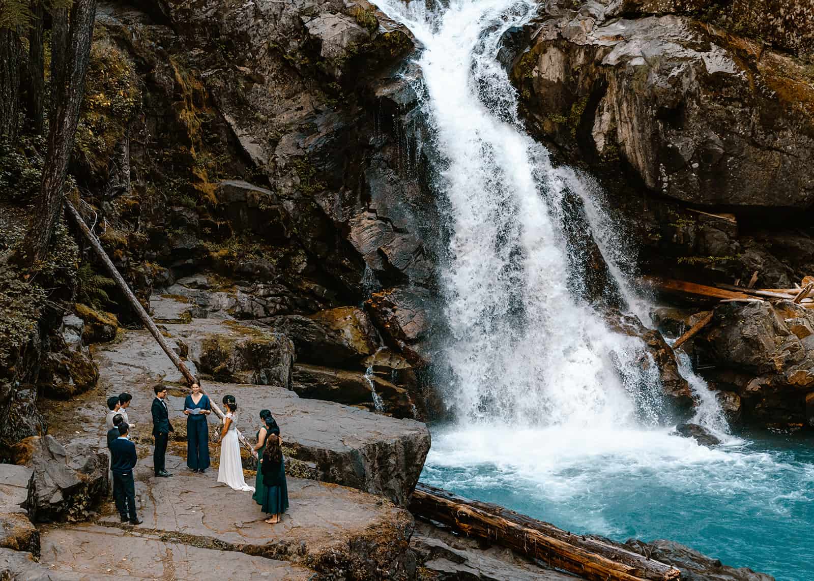 Bride and groom exchange vows with their wedding party infant of a bright blue waterfall as their Oregon elopement photographer takes their photo