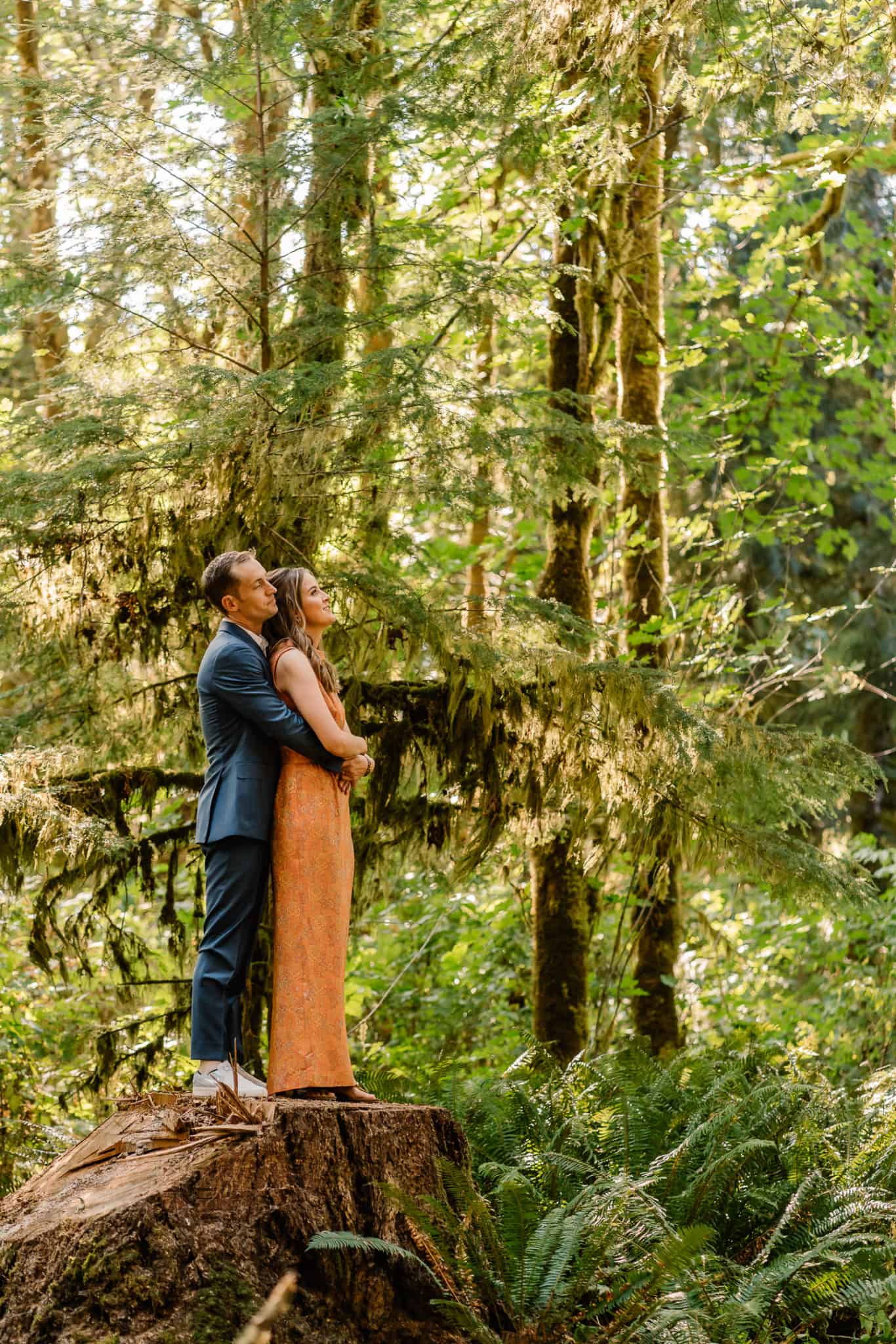 Couple embraces in their favorite Oregon elopement location deep in the forest on a large tree stump