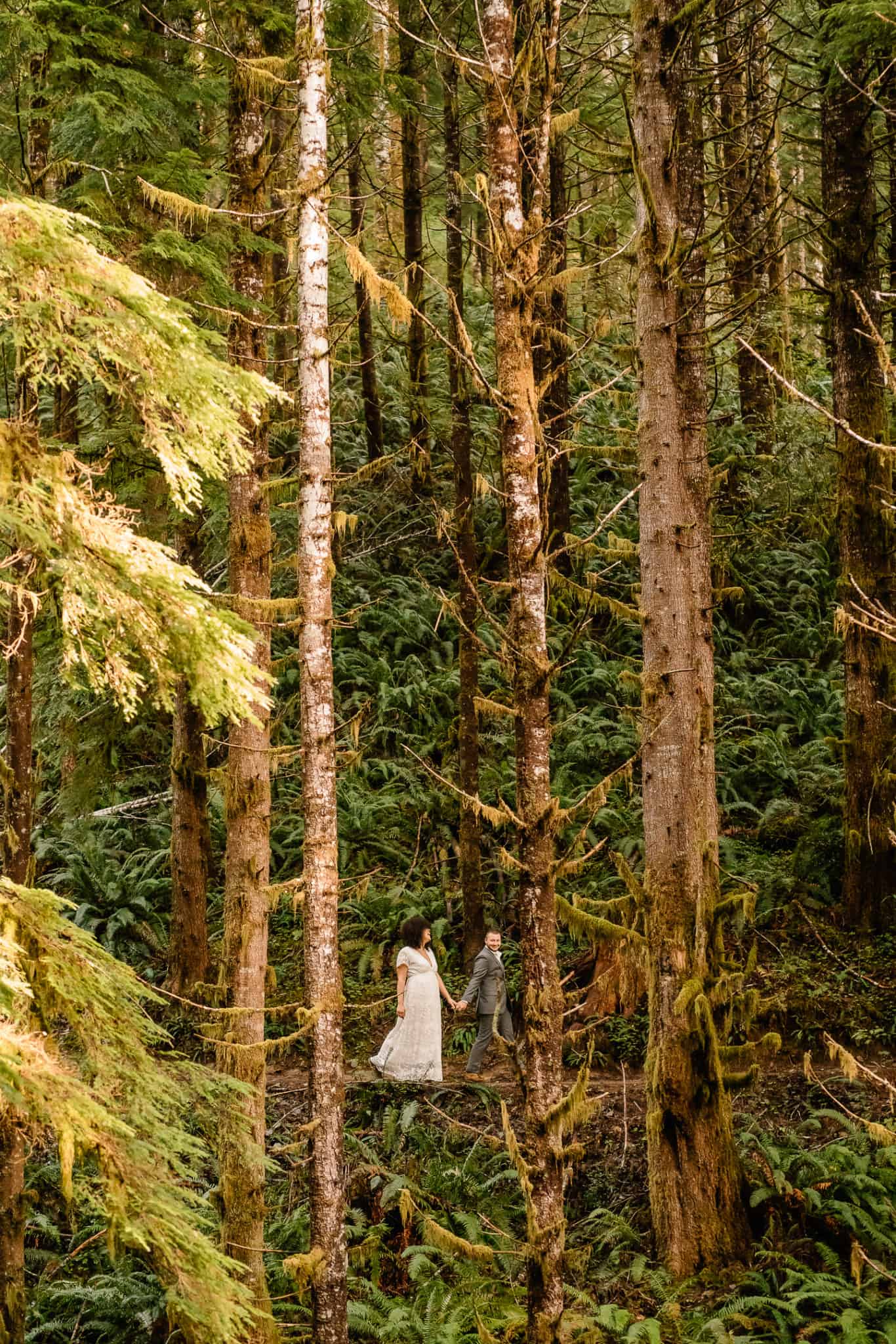 Couple walks through the forest in one of the best places to elope in Oregon surrounded by trees and greenery
