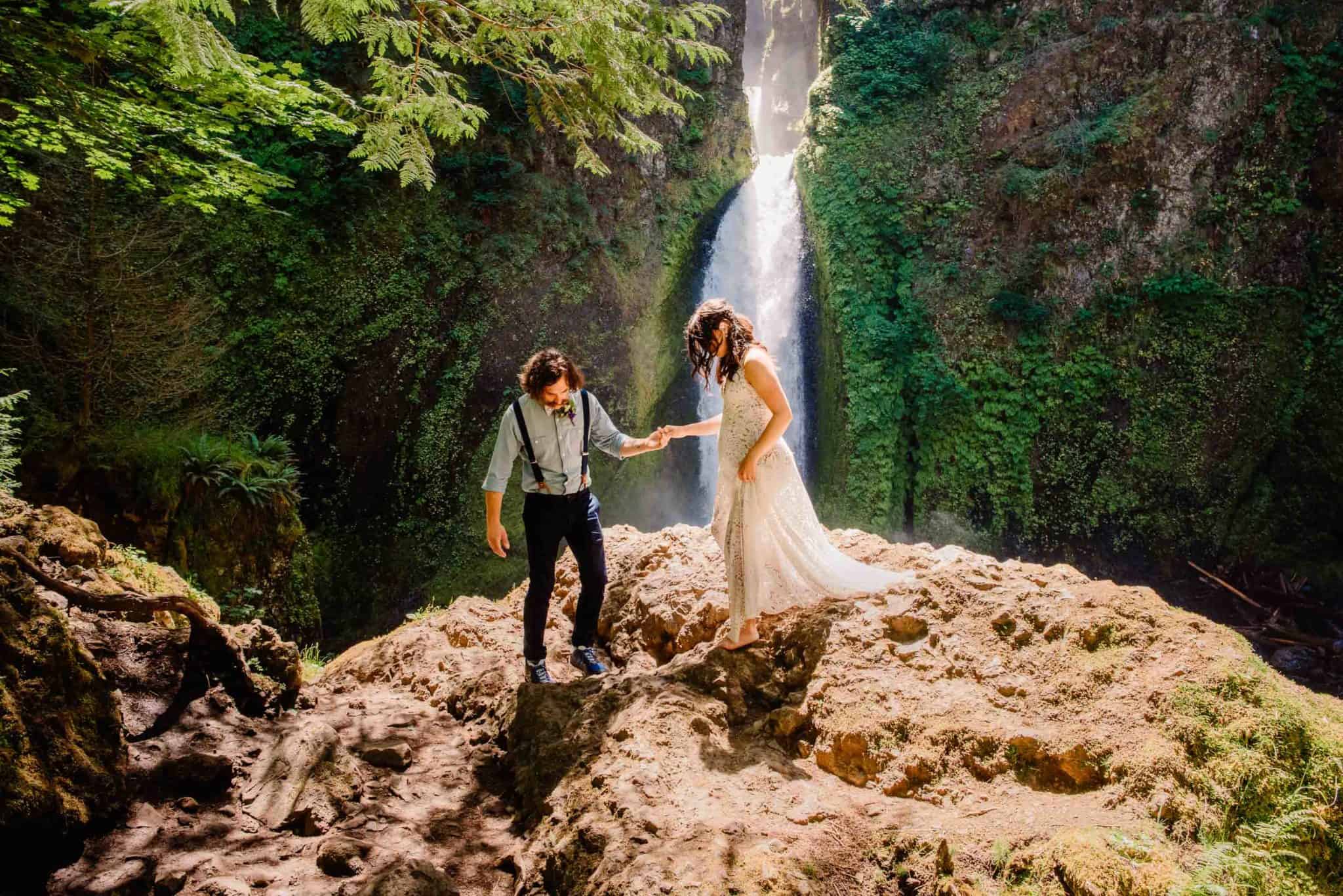 Couple explores a waterfall on a rock drenched in sunlight after learning how to elope in Oregon