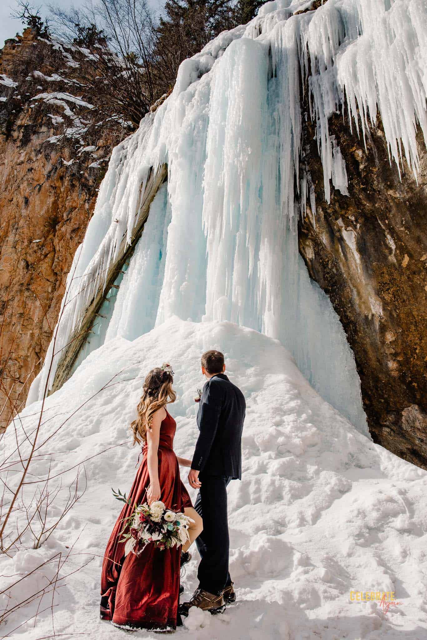 couple eloping in Colorado during the winter looking at a froze waterfall before they go get in the hot springs