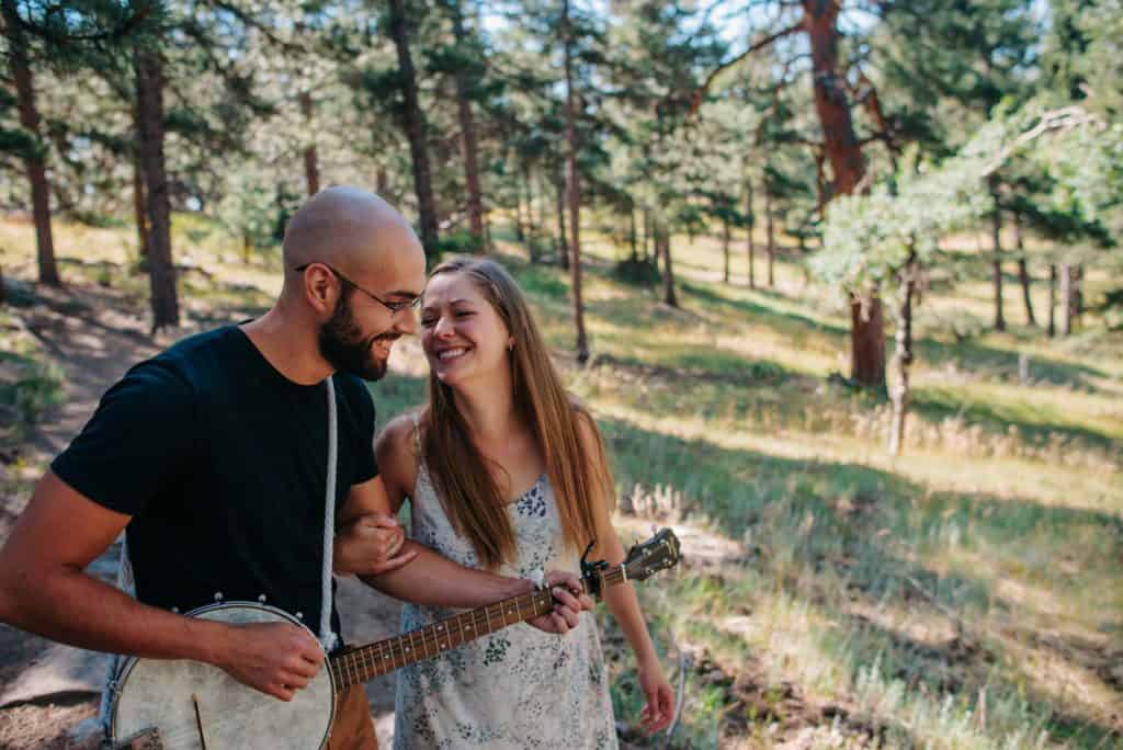 couple smiling at each other while one partner plays an instrument in the forest during a couples connection experience