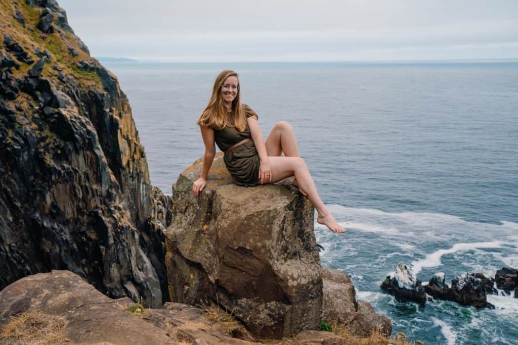 On an ocean cliff side Lumalia sits on a rock with her barefeet
