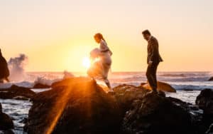 A couple in their wedding attire and their Oregon elopement photographer climb sea stacks during sunset