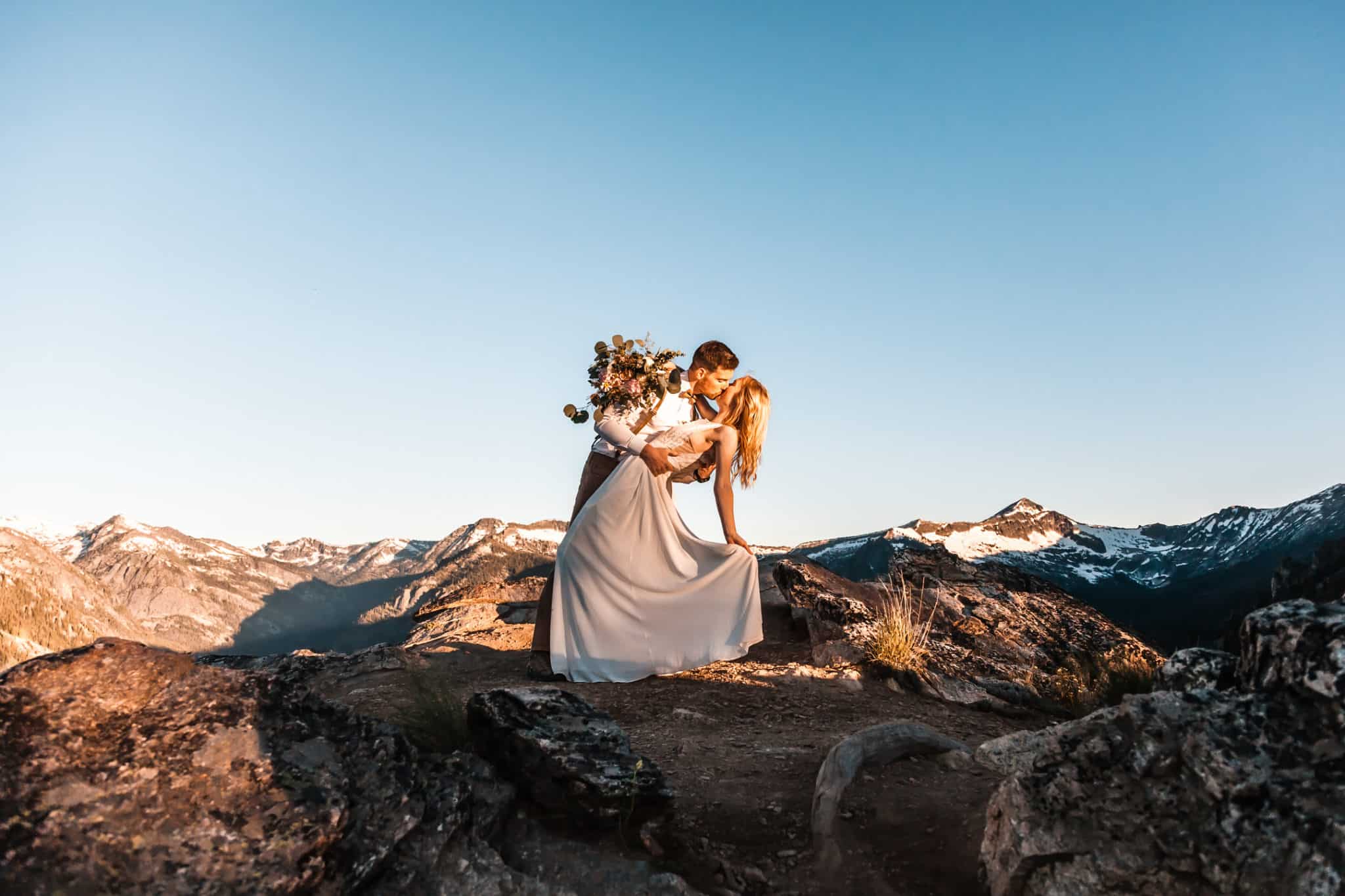couples kissing on a mountain top at sunset as bride lifts her dress up making a perfect Colorado elopement package moment