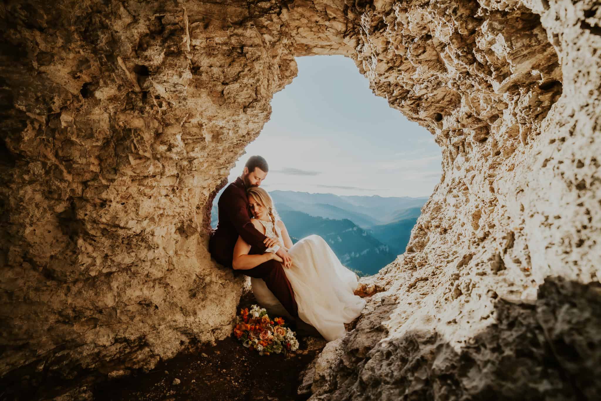 couple sitting inside a hole in a rock with mountains in the background on their Colorado elopement wedding day