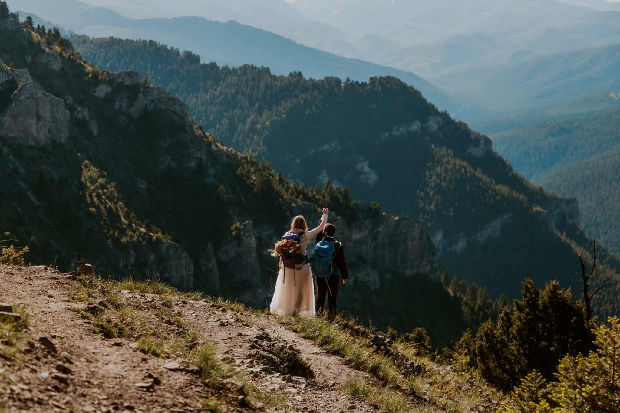 couple cheering as they are walking down a mountain in wedding attire and wearing backpacks for their Oregon elopement package
