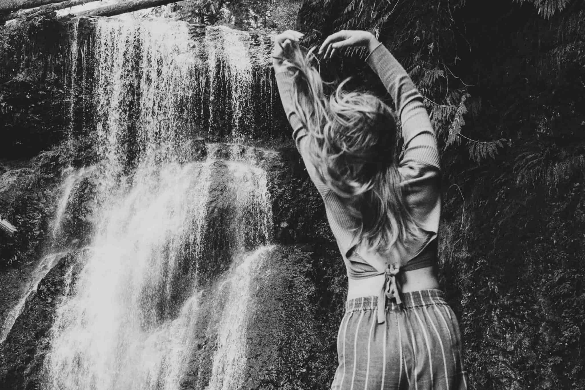 hands reaching to sky near a waterfall with feminine movement exploring sexuality