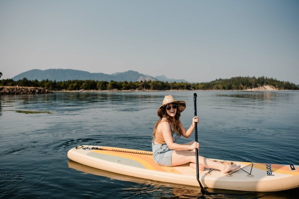 female on a paddlebaord smiling on the Oregon Coast a wellness retreat in Oregon