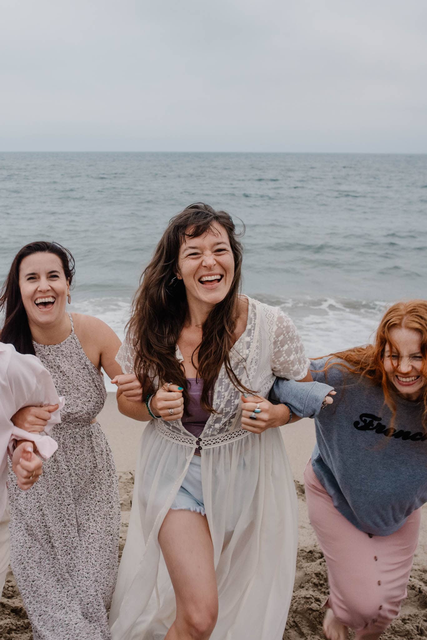 women smiling a women's retreat in Oregon on the beach hooking arms together
