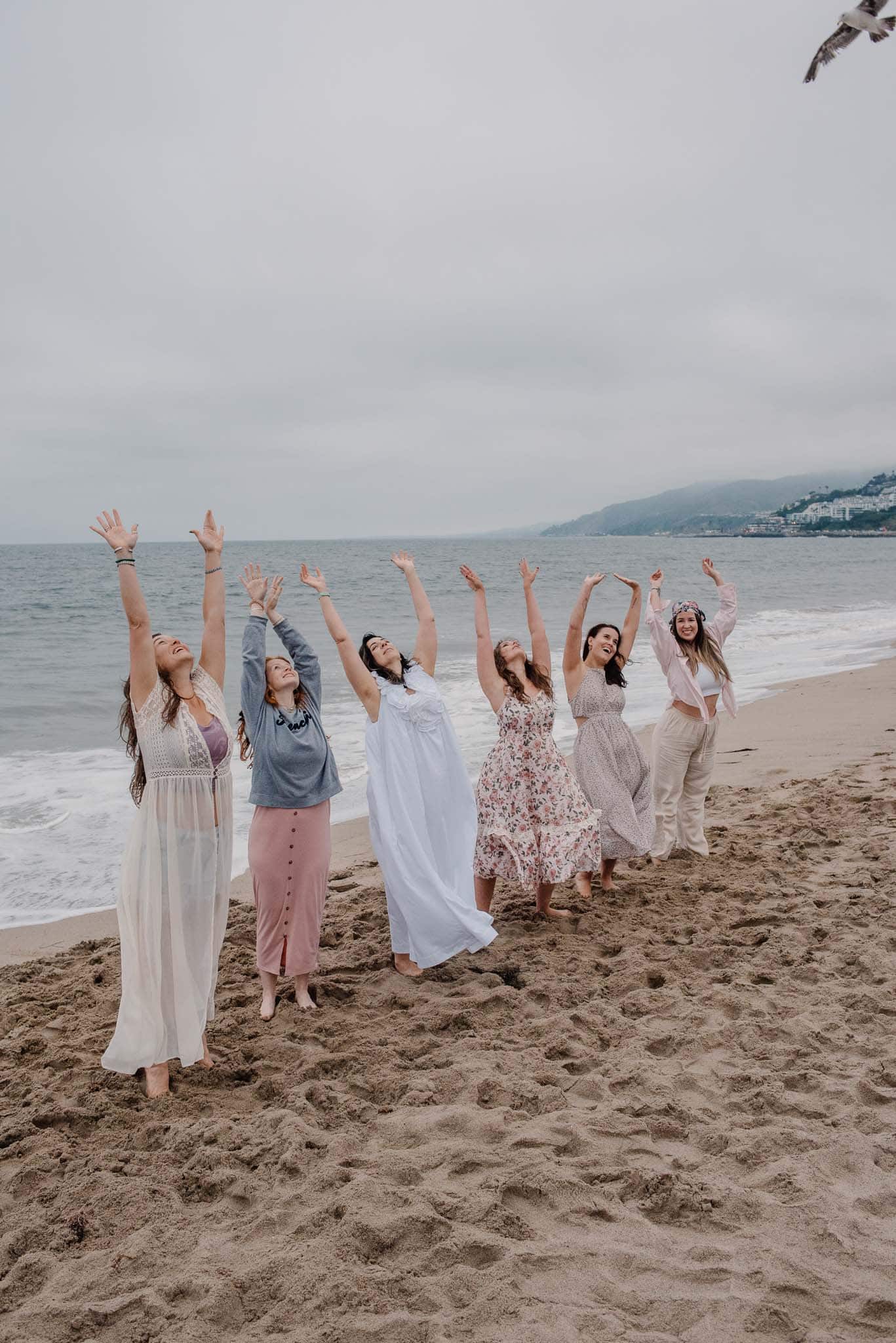 women raising arms up at community boudior photography gathering on the Oregon coast