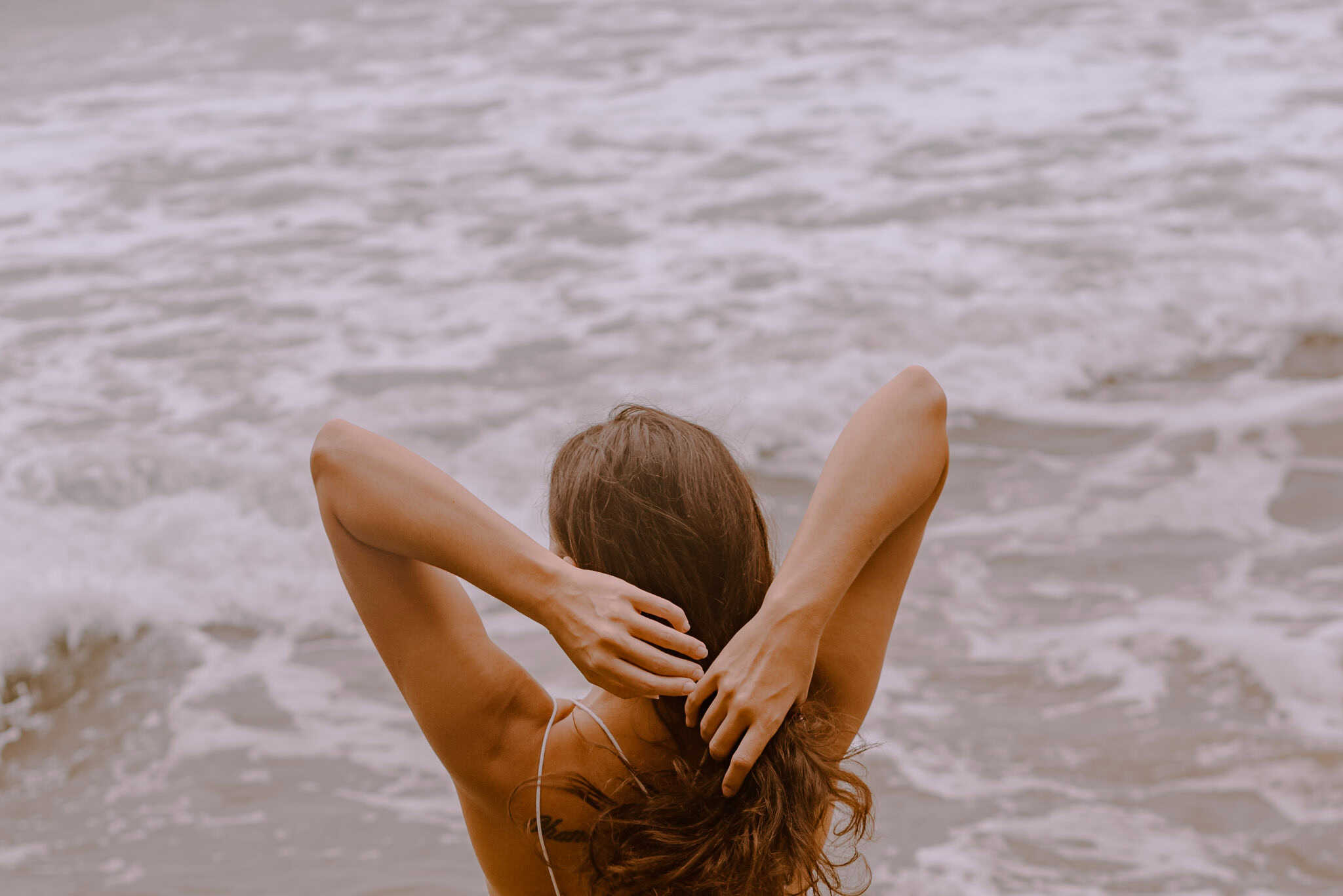 person tying their hair back in front of an ocean for some self care