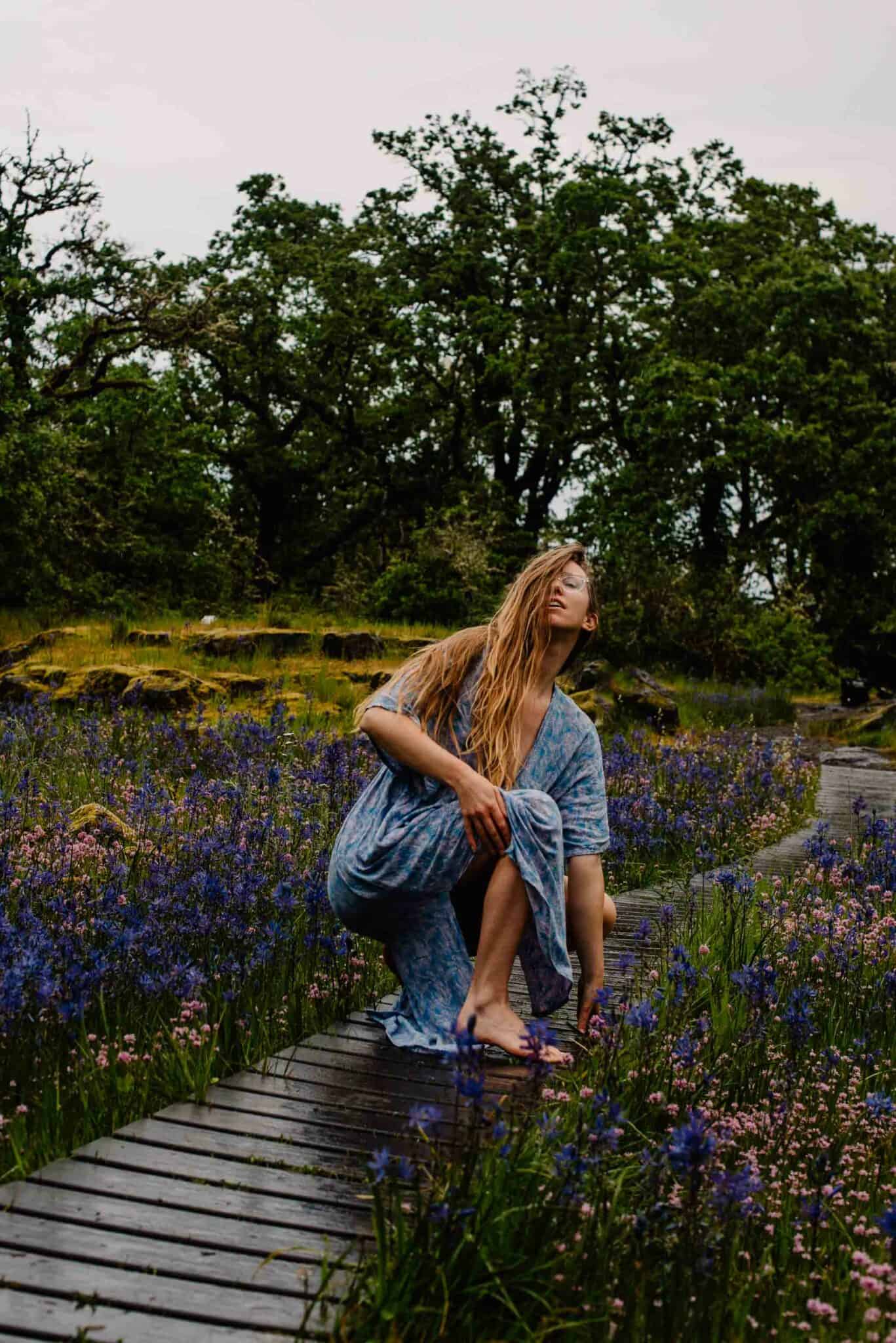 Lumalia as the siren archetype standing near wild flowers on a rainy trail