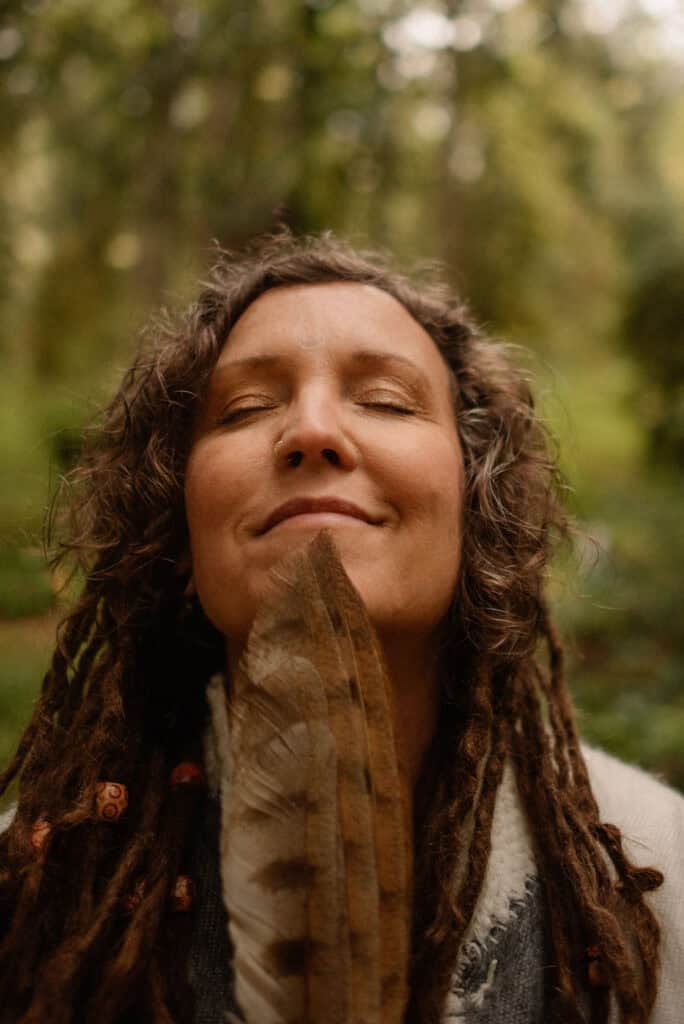 woman holding leaf up to face in a forest after learning how to reconnect with yoruself when you feel lost