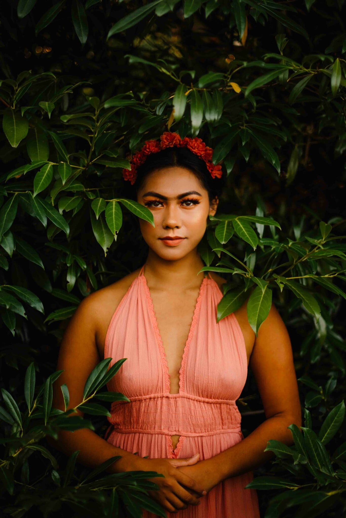 frida kahlo inspired female portrait photography by Portland Oregon photographer female in pink dress with flowers on her hair and make up like Frida Kahlo standing around bushes