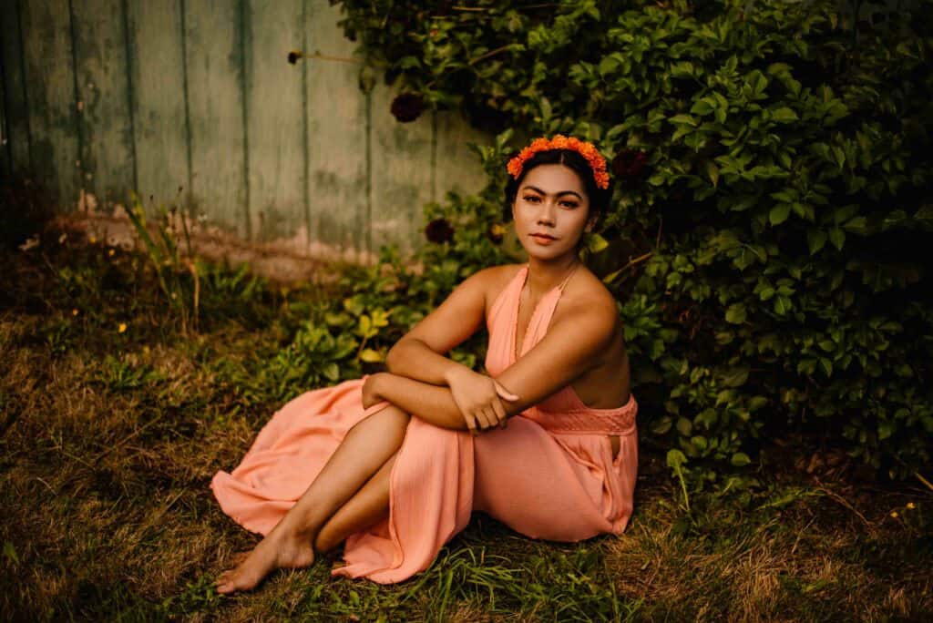 frida kahlo inspired female portrait photography by Portland Oregon photographer female in pink dress with flowers on her hair and make up like Frida Kahlo sits on the ground barefoot with her legs extended