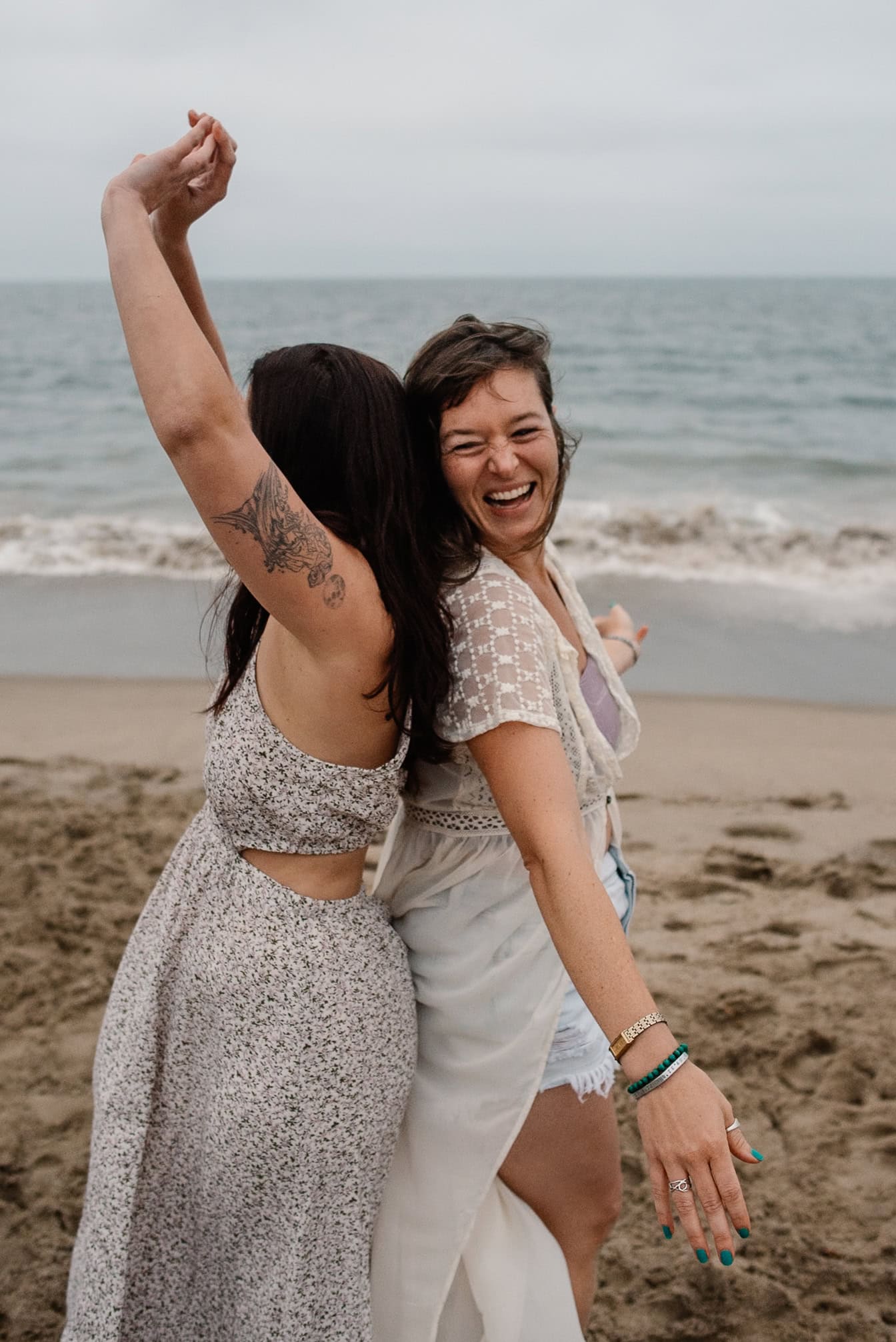 women laughing back to back by the ocean as they heal the sister wound during a women's retreat