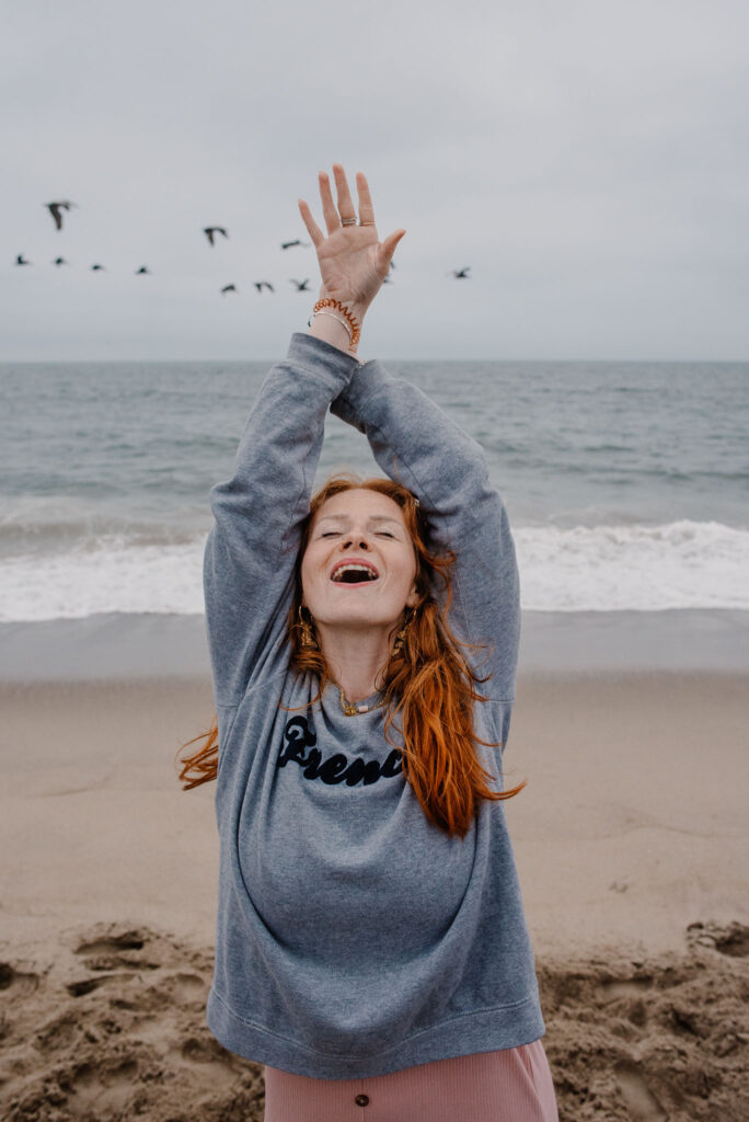 woman raising arms with birds flying behind her