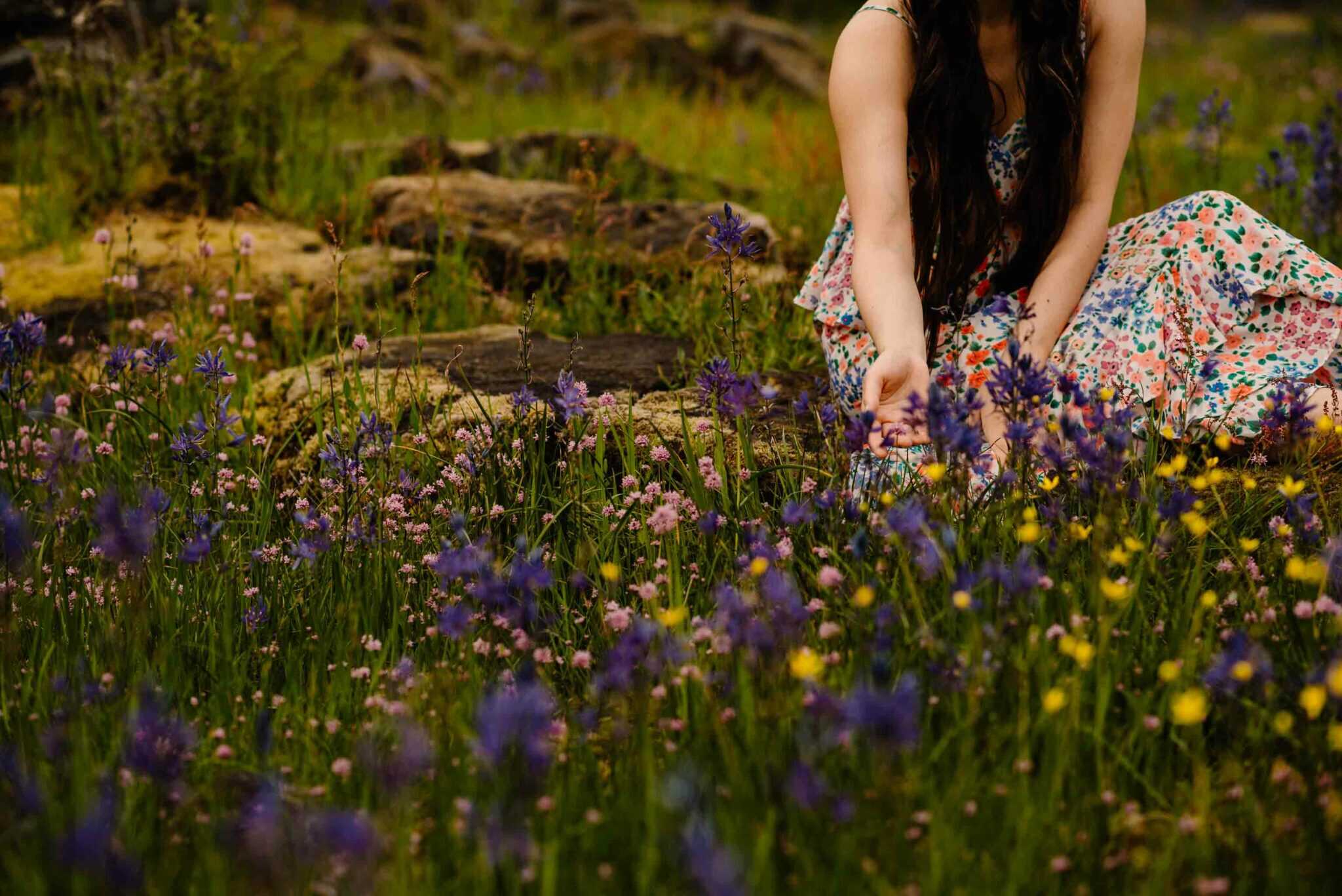 woman on a rock reaching towards wild flowers