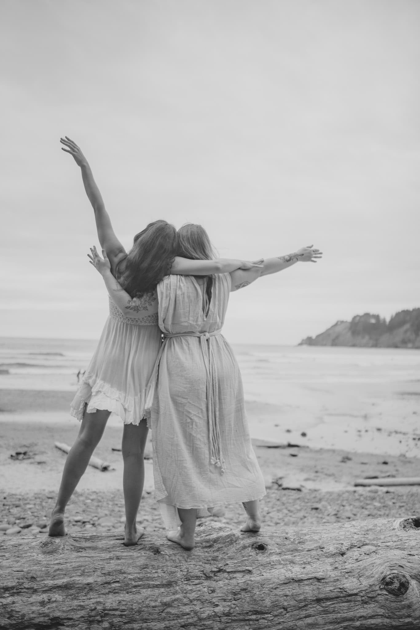 girls holding arms on a log near the ocean